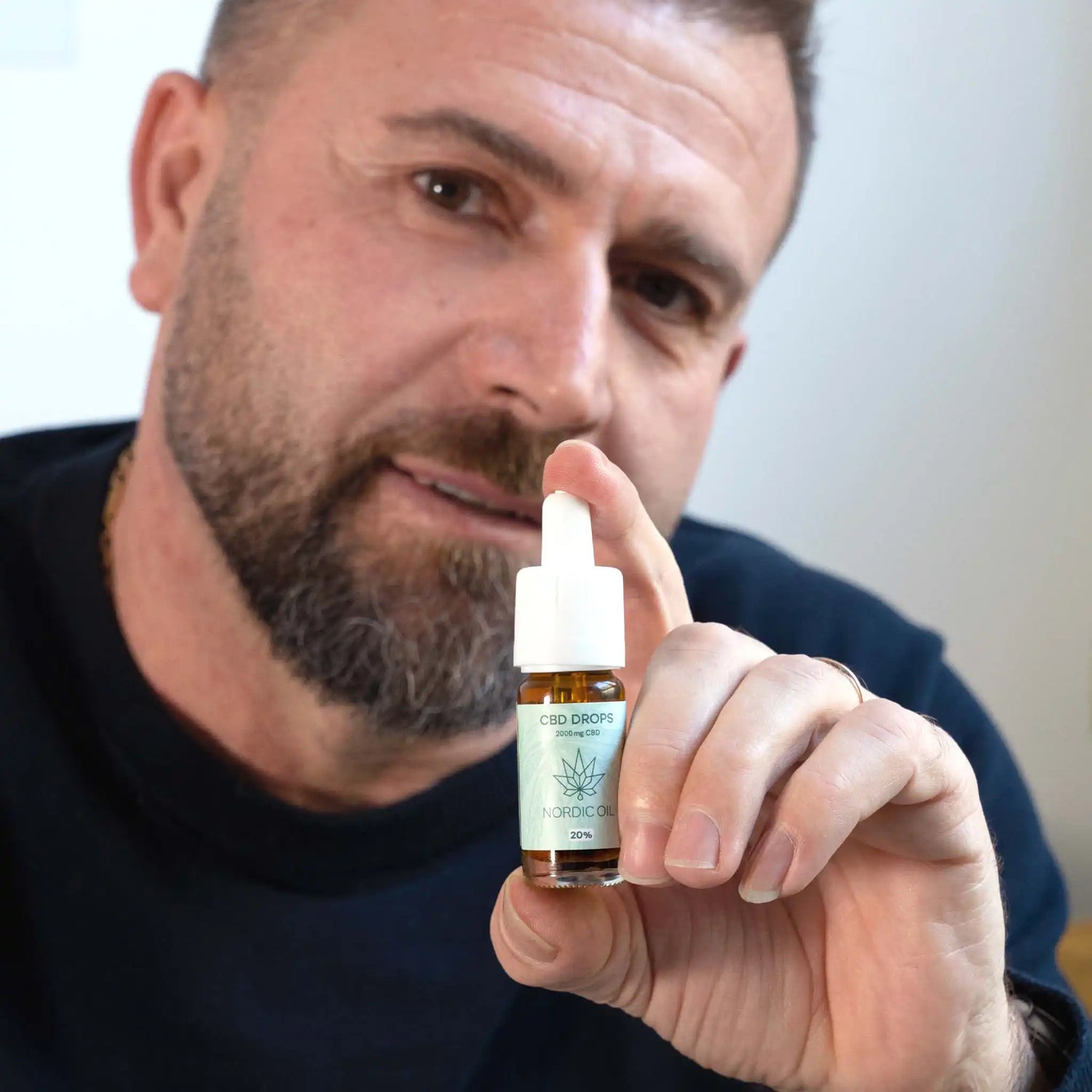 een man houdt de CBD olie in de camera terwijl hij glimlacht