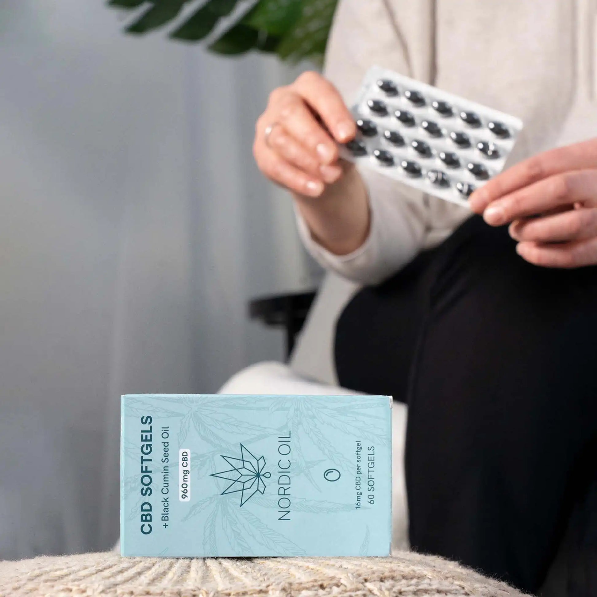 Op de voorgrond de verpakking van CBD-capsules; op de achtergrond houdt de klant de capsules vast.